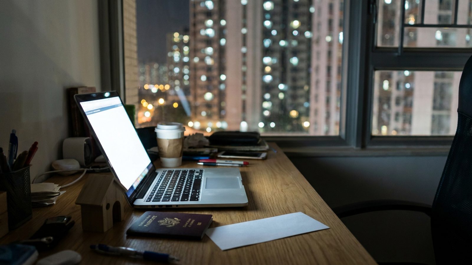An overseas Filipino worker's desk at night with a laptop, passport and a small model house, city lights outside